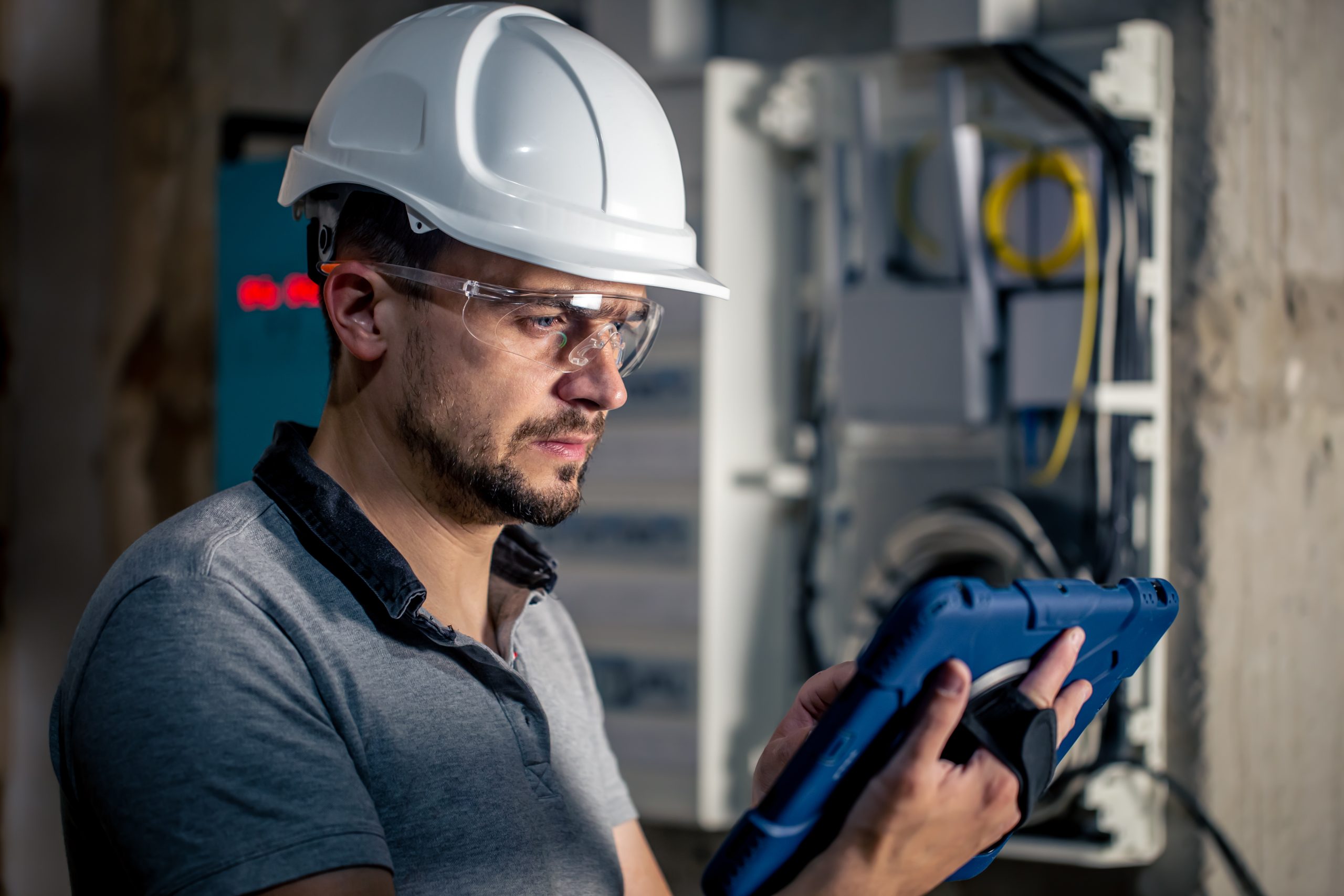 Man, an electrical technician working in a switchboard with fuses, uses a tablet.